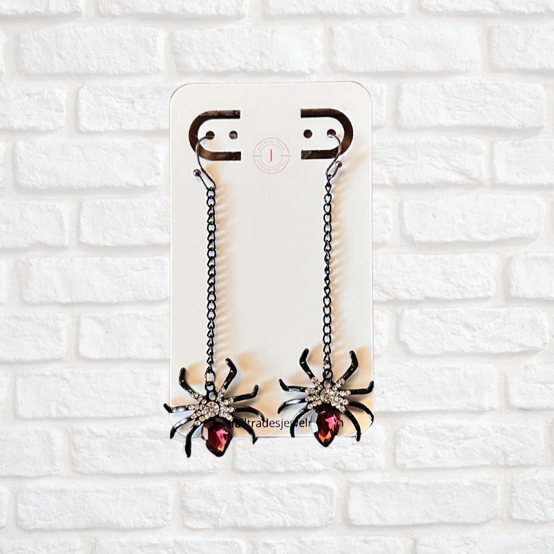 Pair of spider-shaped earrings on a white brick wall background