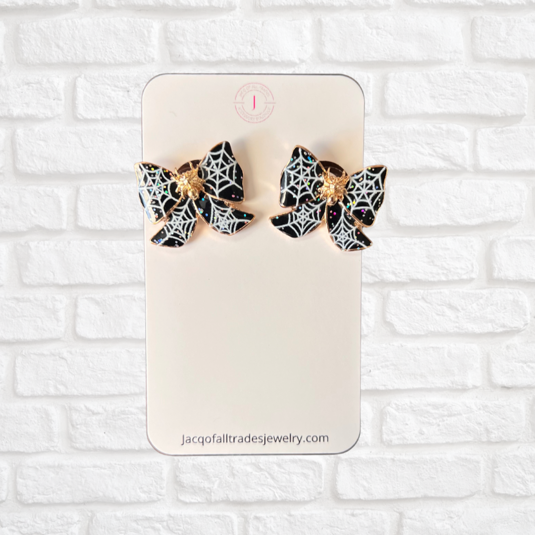 Spider web earrings on a display card against a white brick wall background