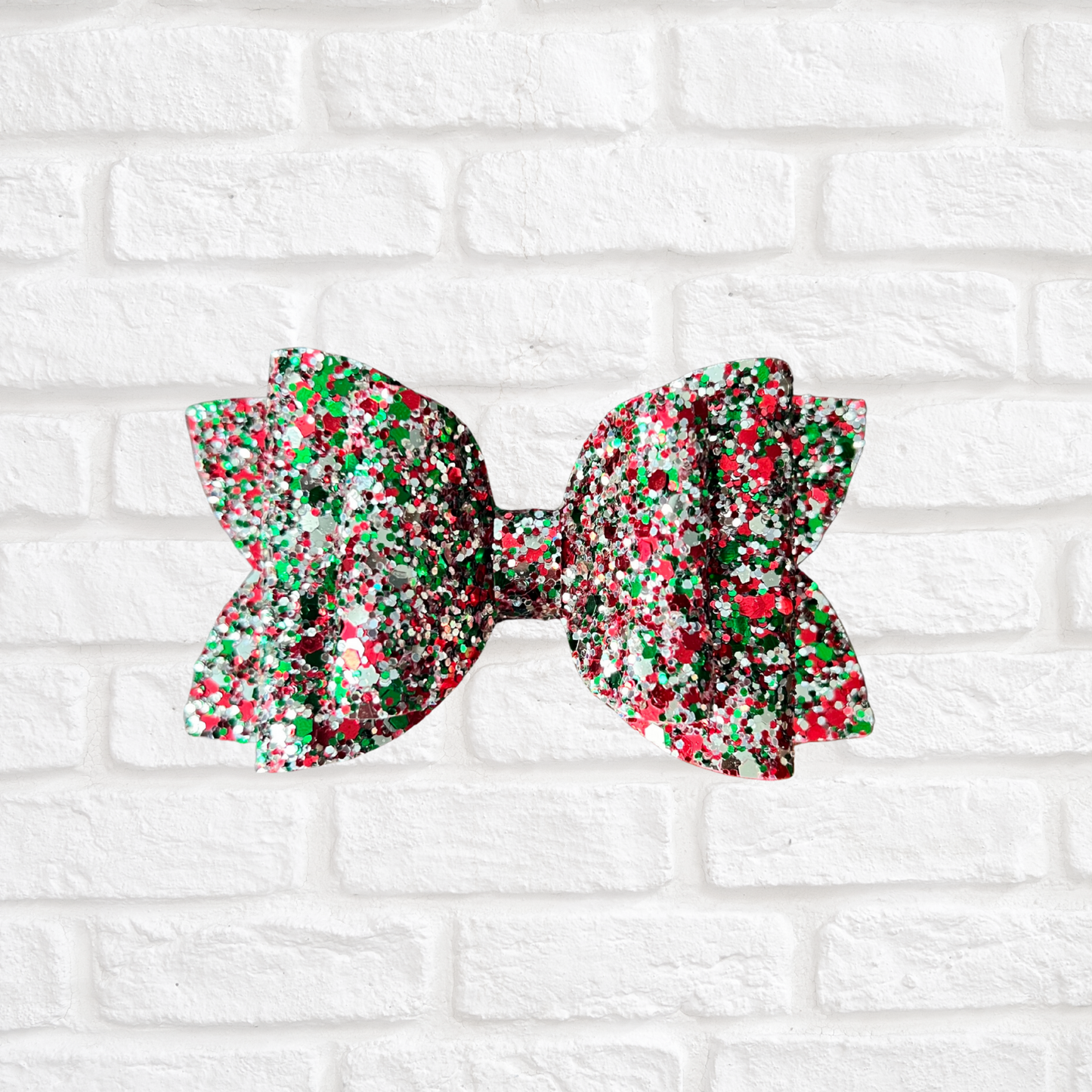 Red, green, and white glittery bow on a white brick wall background