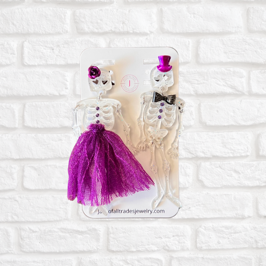 Pair of skeleton earrings with purple accents on a white brick background
