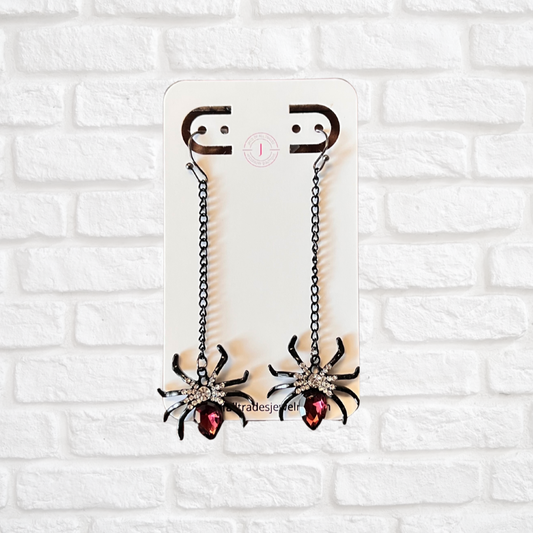 Pair of spider-shaped earrings on a white brick wall background