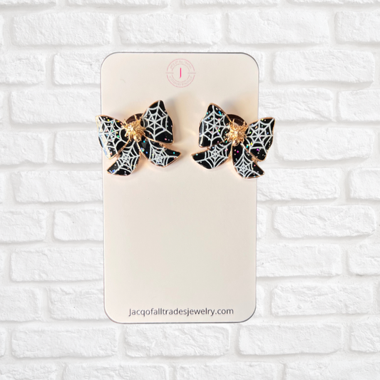 Spider web earrings on a display card against a white brick wall background